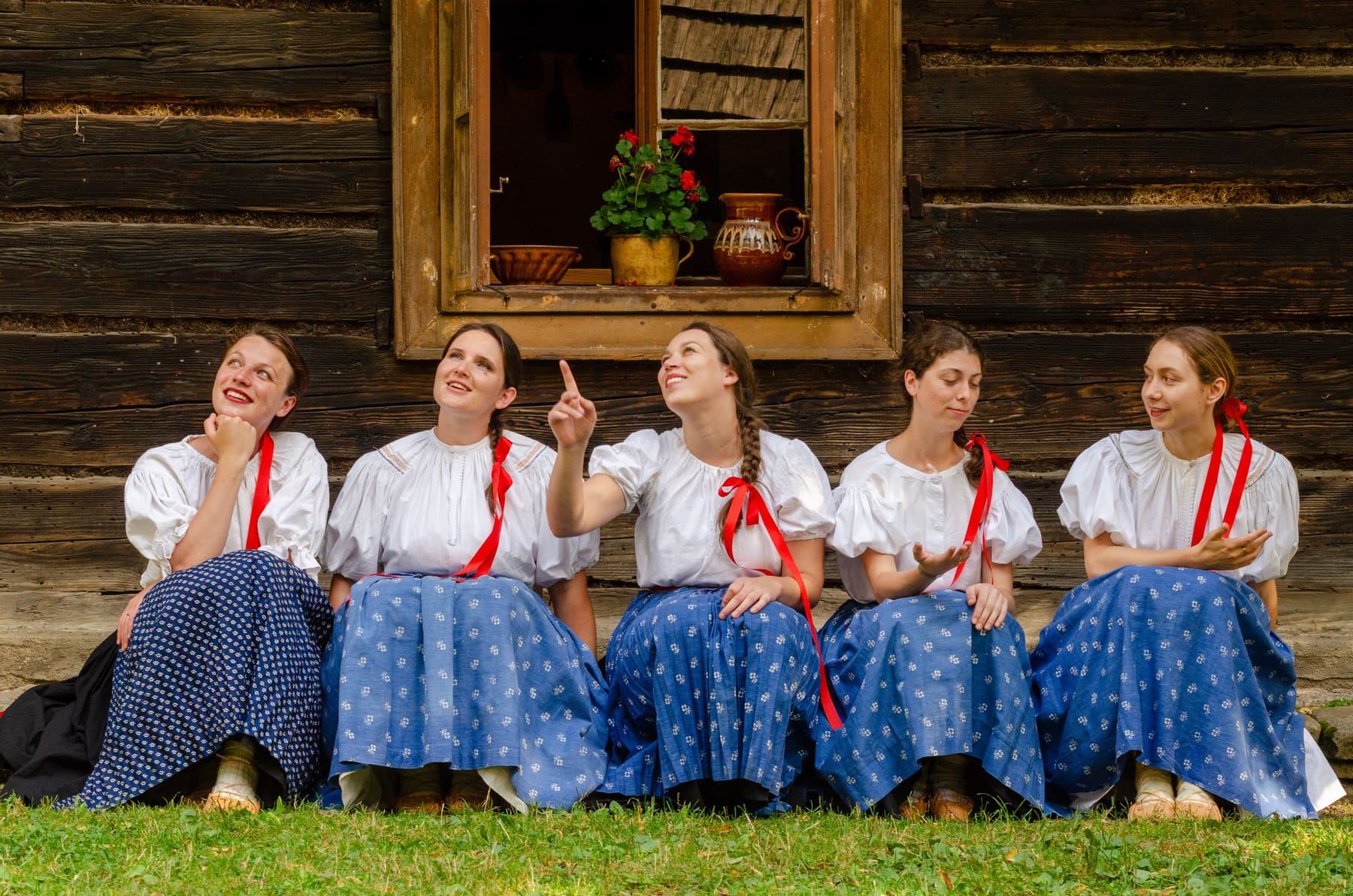 Členky cimbálové muziky Parádnica v hanáckém kroji sedí před roubenkou